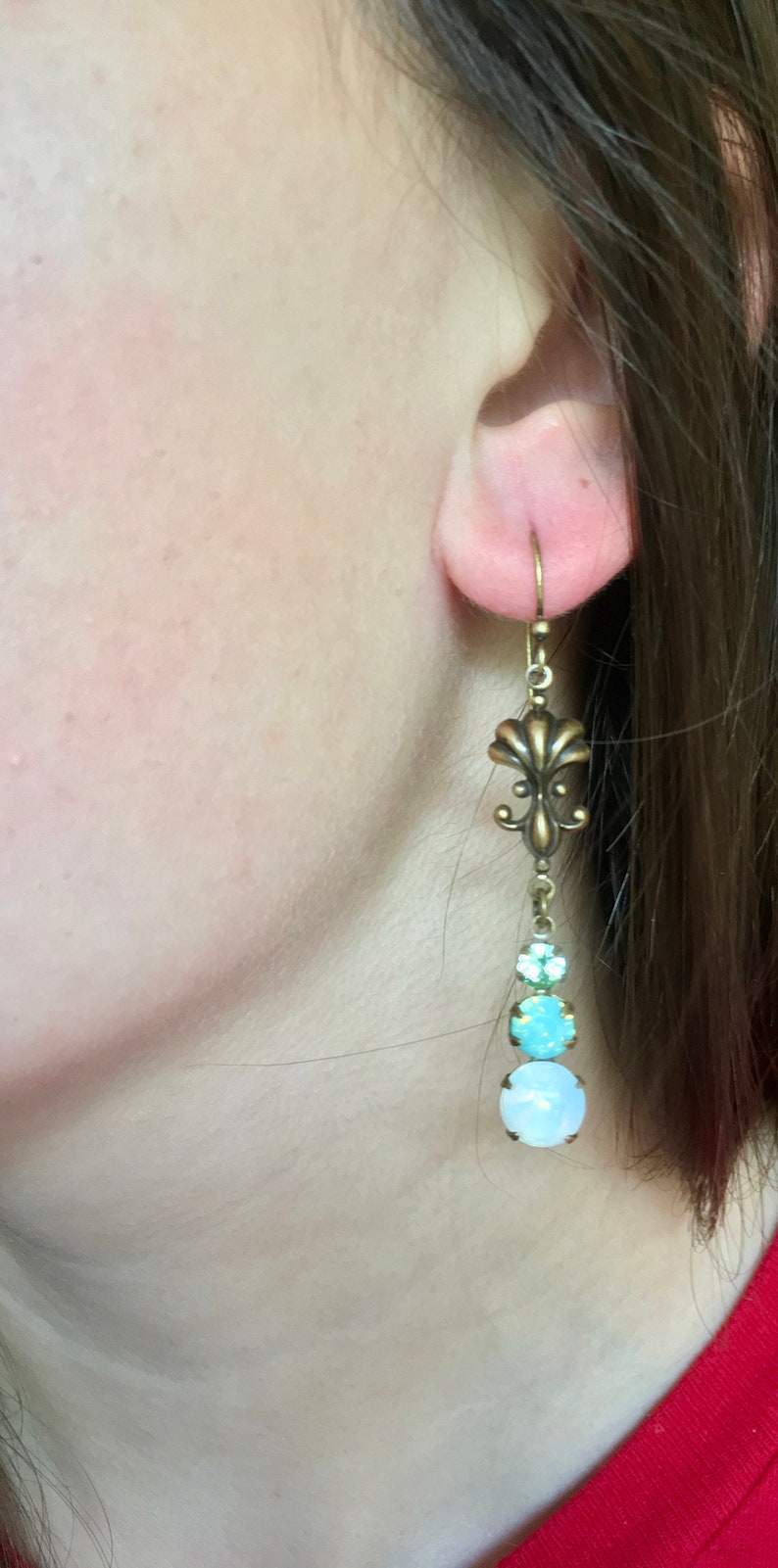 May include: Brass earrings with a fleur-de-lis design and three round, iridescent stones in shades of blue and white.