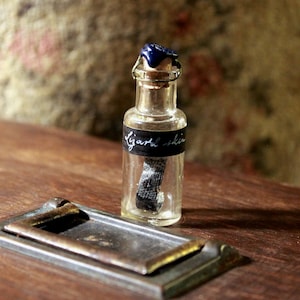 May include: A small glass bottle with a blue stopper and a black label that reads "Lizard Skin". The bottle is sitting on a wooden surface.