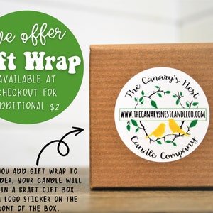May include: A brown kraft gift box with a white sticker featuring a logo of two yellow birds on a branch with green leaves. The text on the sticker reads "The Canary's Nest Candle Company" and "www.thecanarysnestcandleco.com". A green circle with white text reads "We offer Gift Wrap Available at Checkout for Additional $2".