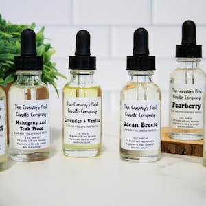 May include: Seven glass bottles of car air freshener refills with black dropper tops and white labels. The labels have the company name "The Canary's Nest Candle Company" and the scent names: "Fiji Sunset", "Mahogany and Teak Wood", "Lavender + Vanilla", "Ocean Breeze", "Pearberry", "Mahogany Coconut".