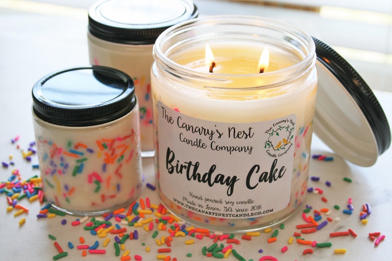 Clear, sleek jar candle with black lid. The candle scent is Birthday Cake and the wax is white with rainbow sprinkles around the edges of the jar.