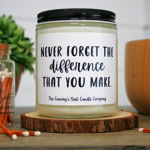 May include: A white candle with a black lid and a label that reads "Never forget the difference that you make." The label also includes the text "The Canary's Nest Candle Company".