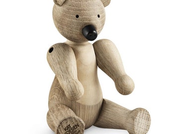 Puede incluir: Un juguete de oso de madera con la nariz negra y un acabado marrón. El oso está sentado con las piernas extendidas. El oso está hecho por Kay Bojesen Design y tiene un aviso de copyright en la parte inferior de su pie.