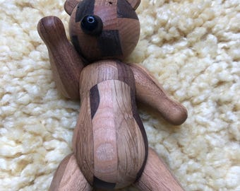 Puede incluir: Un juguete de oso de madera con un diseño de patchwork hecho de diferentes tipos de madera. El oso está de pie sobre sus cuatro patas con los brazos levantados. El oso tiene una nariz negra y ojos negros.