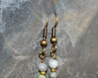 May include: A pair of handcrafted earrings with a vintage aesthetic. Each earring features a gold-colored hook, a coiled spring, and a series of beads in shades of gray, green, and deep red. The beads are strung together with gold-colored wire.