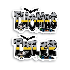 May include: Two black and yellow Batman-themed name decals with a bat silhouette, a small Batman character, and a Batmobile. The names are "Thomas" and "Tyler".