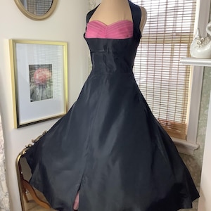 May include: A black halter dress with a pink bodice, displayed on a mannequin. The dress has a full skirt and a slit in the front. A silver necklace is around the mannequin's neck.