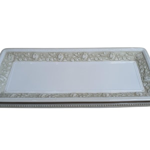 May include: A rectangular, off-white ceramic serving tray with a raised floral border. The border features detailed rose and leaf designs in a muted, neutral color. The tray has a smooth, rectangular center.