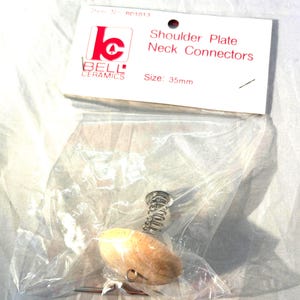 May include: A package containing a shoulder plate neck connector. The package includes a wooden-colored oval piece, a silver spring, and a metal pin. The label reads "Shoulder Plate Neck Connectors" and "Size: 35mm". The brand logo is "Bell Ceramics".
