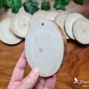 Peut inclure: Gros plan sur un disque rond en bois blanc avec un trou au centre. Le disque est tenu par une main. Le disque fait partie d'un ensemble de disques en bois.
