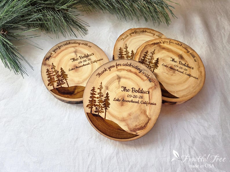 May include: Four circular wooden coasters with natural bark edges, each laser-engraved with a pine tree forest graphic, the text "Thank you for celebrating with us," "The Bolducs," "09-26-26," and "Lake Arrowhead, California" in dark brown ink.