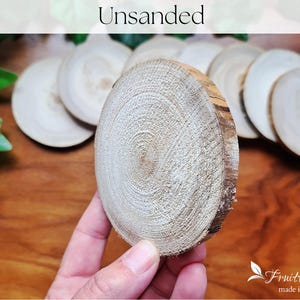 May include: Unsanded wood slices, a close-up of a single slice with a natural wood grain pattern. The wood is light in colour and has a rough, unfinished texture.