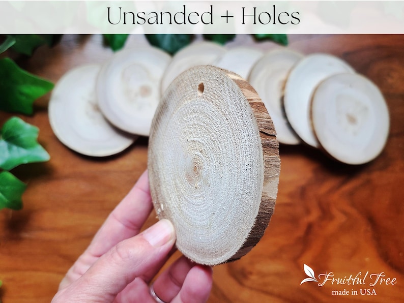 May include: A close-up of a pile of unfinished wood slices with holes drilled in the centre. The wood is a light brown colour and has a natural, rustic look. The slices are arranged in a pile, with the top slice being held in a hand.