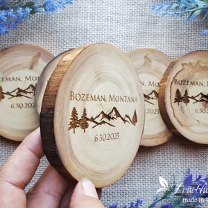 May include: Four circular wood slices with natural bark edges, each engraved with a mountain range, pine trees, the text BOZEMAN, MONTANA, and the date 6.30.2023. The wood features visible grain patterns and light brown tones throughout the surface.