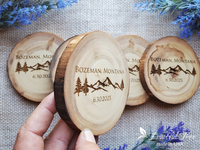 May include: Four circular wood slices with natural bark edges, each engraved with a mountain range, pine trees, the text BOZEMAN, MONTANA, and the date 6.30.2023. The wood features visible grain patterns and light brown tones throughout the surface.