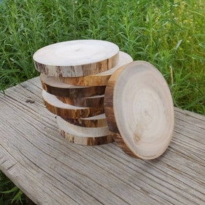 May include: A stack of six round wooden slices, each with a different wood grain pattern. The slices are arranged in a pile, with the largest slice on the bottom and the smallest slice on top. The slices are all natural wood, with no paint or stain.