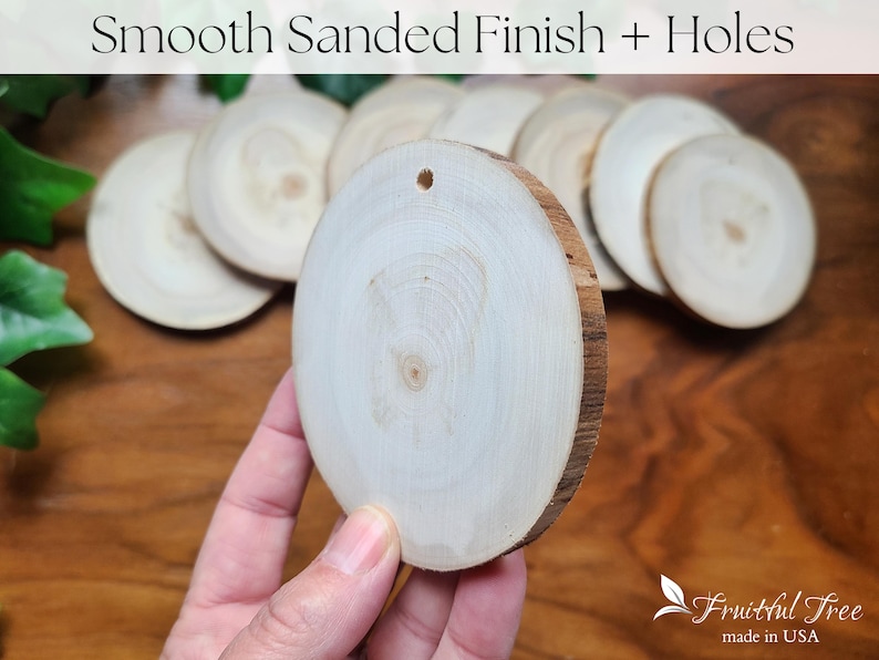 May include: A close-up of a smooth, sanded, white wood round with a hole in the centre. The round is being held in a hand. The wood is smooth and has a natural grain pattern. The round is surrounded by other similar rounds.