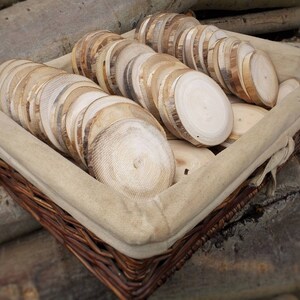 This shows a basket of about 50 aspen wood slices with no bark. Over time the bark has fallen off leaving the edge dark brown and grey in color. This wood slice is unfinished, leaving a rough surface from cutting by hand.