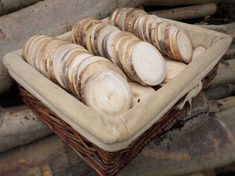 This shows a basket of about 50 aspen wood slices with no bark. Over time the bark has fallen off leaving the edge dark brown and grey in color. This wood slice is unfinished, leaving a rough surface from cutting by hand.