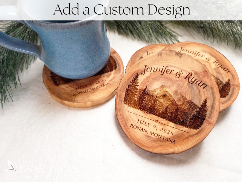 May include: Round wooden coasters featuring a laser-engraved mountain and pine tree landscape. The text reads Jennifer & Ryan, July 9, 2026, and Ronan, Montana. A blue ceramic mug sits on one coaster, and the image includes the text Add a Custom Design.