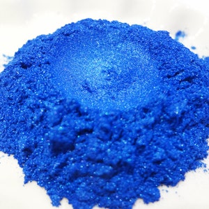 Puede incluir: Un mont&oacute;n de polvo de pigmento azul brillante con purpurina. El polvo es fino y brillante, con un ligero brillo iridiscente.