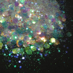 May include: A pile of iridescent glitter in various shades of green, blue, and purple. The glitter is scattered on a black background.