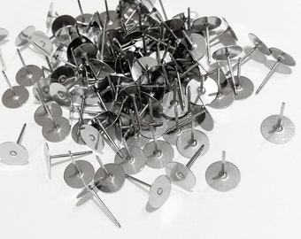 May include: A large pile of silver earring posts with flat round backs. The posts are scattered on a white surface.