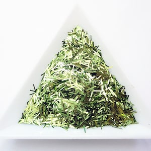 May include: A pile of green and gold glitter in a white triangular container.