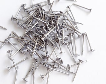 May include: A pile of silver-toned metal earring posts with flat round tops.