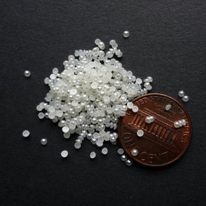 May include: A pile of small, white pearl-like beads next to a US penny. The penny is face up and shows the Lincoln Memorial and the words "United States of America, One Cent".