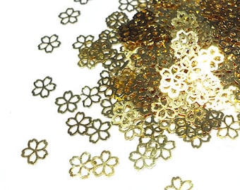 May include: A pile of gold metal flower-shaped embellishments, scattered on a white background.
