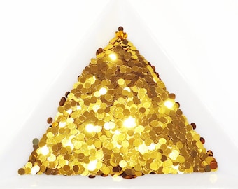 May include: A white triangular tray filled with gold glitter. The glitter is arranged in a pyramid shape.