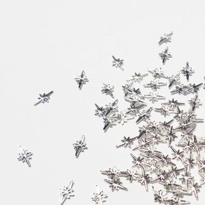 May include: A scattering of silver star-shaped nail charms on a white background.