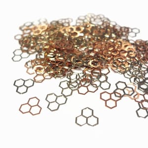 May include: A pile of gold and rose gold honeycomb shaped glitter. The glitter is scattered on a white background.