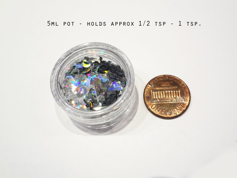 K&ouml;nnte beinhalten: Ein kleines, klares Plastikglas gef&uuml;llt mit schimmerndem silbernen und schwarzen Glitter. Das Glas ist etwa so gro&szlig; wie ein 1-Cent-St&uuml;ck.