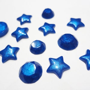 Puede incluir: Una colecci&oacute;n de cabujones de resina de color azul en forma de estrella y redonda con un acabado brillante.
