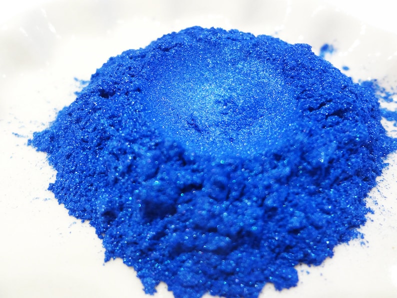 Puede incluir: Un mont&oacute;n de polvo de pigmento azul brillante con purpurina. El polvo es fino y brillante, con un ligero brillo iridiscente.