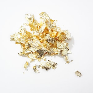 May include: A pile of gold leaf flakes on a white background.