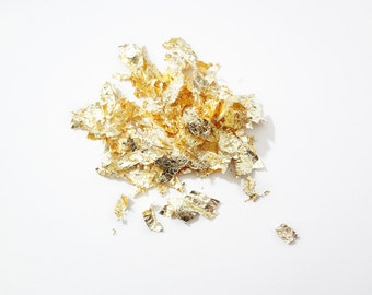 May include: A pile of gold leaf flakes on a white background.