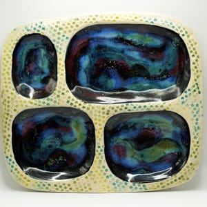 May include: A handmade ceramic serving tray with four compartments. The interior of each compartment features a swirling pattern of blue, green, and red hues. The tray's exterior is off-white with a pattern of small green and yellow stars.