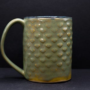 May include: A green ceramic mug with a textured, heart-shaped pattern. The mug has a rounded handle.