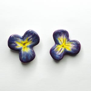 May include: Two handcrafted, violet-blue flower-shaped ceramic pieces with yellow centers. The petals have a glossy finish. These decorative items are likely used as embellishments or small art pieces.