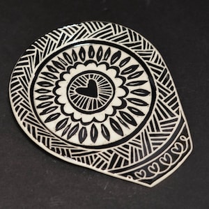 May include: A black and white ceramic dish with a heart-shaped center. The dish features a detailed design of geometric shapes and a heart in the center. The outer edge is decorated with small hearts.