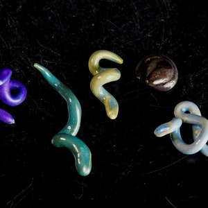 May include: Five ceramic pieces in various shapes and colors. The pieces are in the shape of a snake, a swirl, and a circle. The colors are blue, green, yellow, and brown.