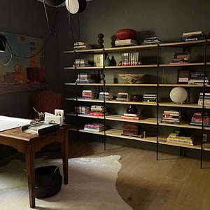 May include: A home office with a wooden desk, a large bookshelf filled with books and decorative items, and a painting on the wall. The room has a modern, minimalist design with a neutral color palette and a cowhide rug.