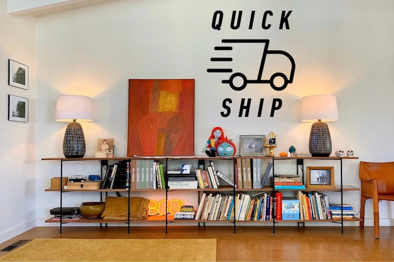 May include: A modern living room setup featuring a long, dark wood shelf unit filled with books, decor, and a neon sign. Two lamps with patterned bases flank the unit. The wall above displays the words "QUICK SHIP" with a graphic of a truck.