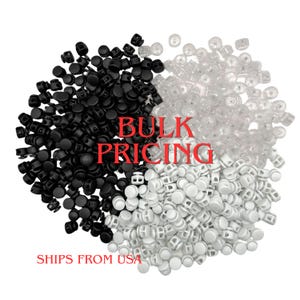 May include: A collection of small plastic cord locks arranged in three distinct color groups: solid black, solid white, and clear. Each cord lock features a cylindrical body with a spring-loaded button mechanism for securing drawstrings.