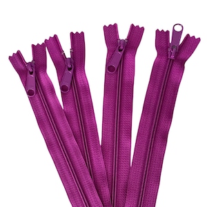 Puede incluir: Primer plano de varias cremalleras de color magenta. Cada cremallera tiene un tirador y dientes a juego. Las cremalleras están dispuestas en forma de abanico sobre un fondo blanco. Ideales para proyectos de costura.