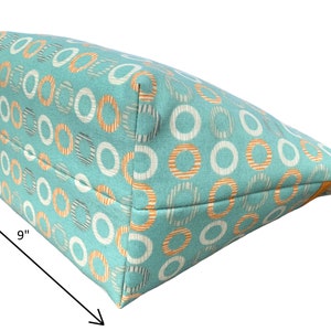 May include: A turquoise tote bag with a white and orange circle pattern. The bag measures 9 inches wide and 6 inches tall.