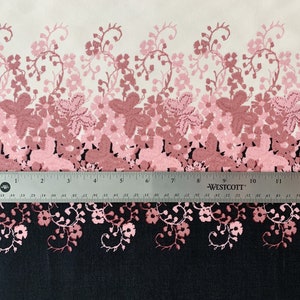May include: A white fabric with a pink and red floral pattern. The pattern is a gradient, with the pink flowers fading to red at the bottom. The fabric is measured with a ruler, showing 12 inches.